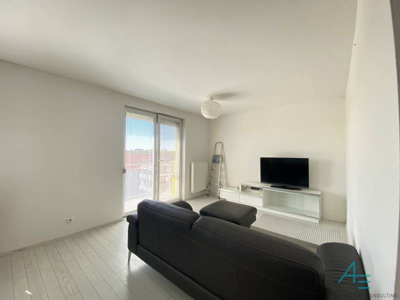 Living room in a 3-room apartment with white walls, TV, and a black sofa.