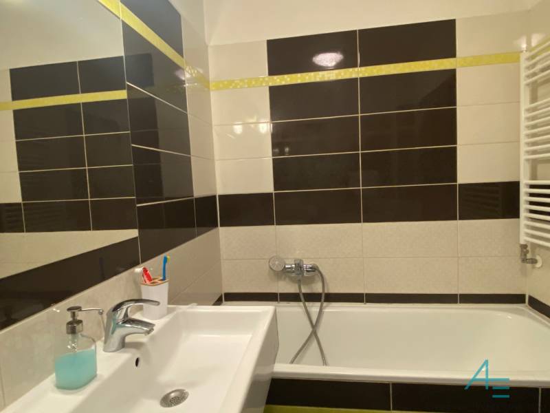 A bathroom in a three-room apartment with a bathtub and a sink, tiled with dark and light tiles.