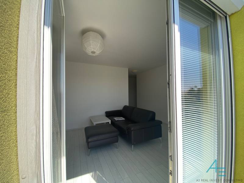 Living room with a sofa in a 3-room apartment, view through open balcony doors.
