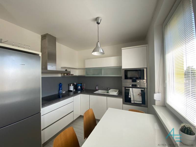 A kitchen in a 3-room apartment with white furniture and appliances, dining table.