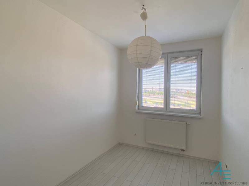 A room in a 3-room apartment with white walls, a hanging lamp, and a window.