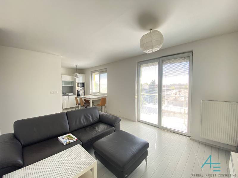 Living room and kitchen in a 3-room apartment with a black sofa, table, and balcony.