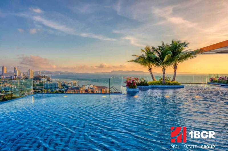 Apartment construction in Pattaya with sea views, a swimming pool, and palm trees on the terrace.