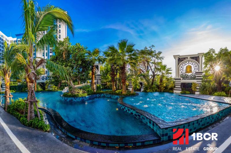 The construction of apartments in Pattaya includes a pool with greenery and palm trees.
