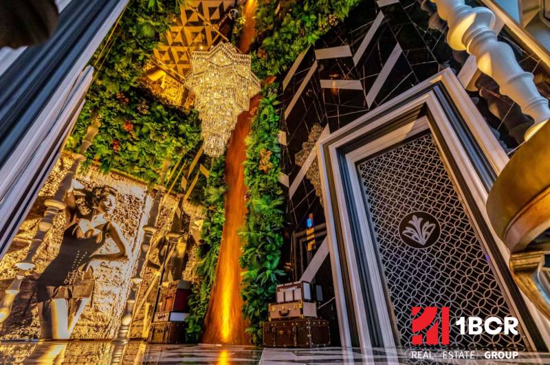 Luxurious interior with a large chandelier, mirrored wall, and green decorations in apartment construction.