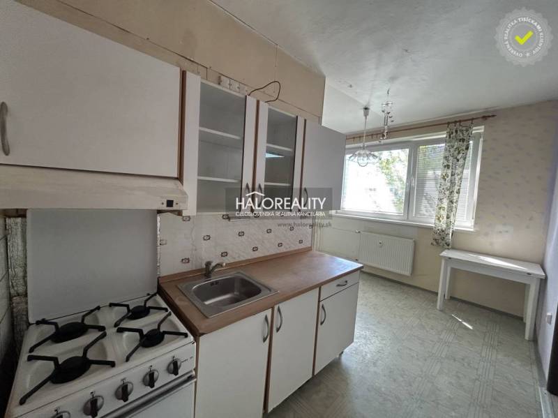 A kitchen with a stove and a sink in a studio apartment, bright furnishings, large window.