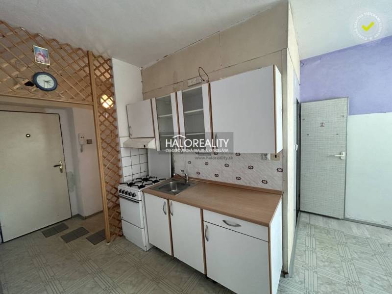 A kitchen in a studio apartment with a gas stove and cabinets, on a white wall.
