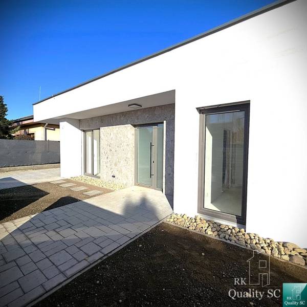 A family house in Turany with a light facade, featuring modern window elements on a paved courtyard.
