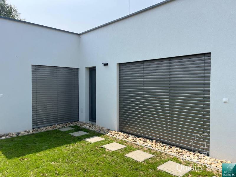 A family house in Turna with a white facade, shutters, and a manicured lawn.