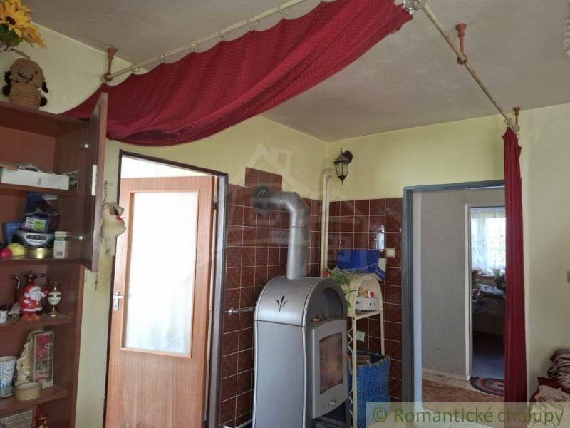 A room in a family house with a stove, curtains, and a shelf full of objects.
