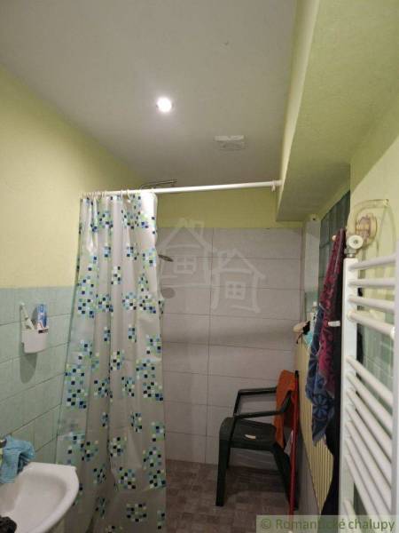 Bathroom in a family house with a bathtub, curtain, and plastic chair.