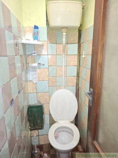 A simple bathroom in a family house with an older toilet and tiles.