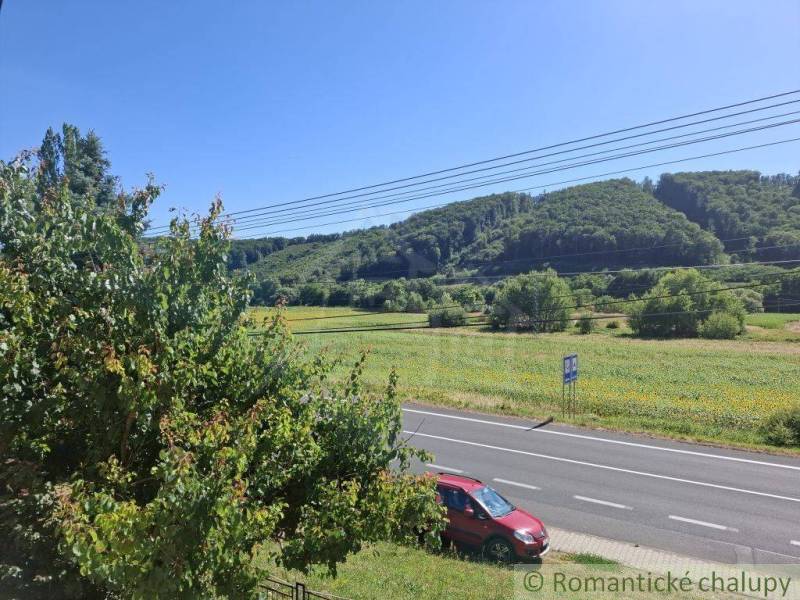 View from a family house in Lovinobaňa, road with a car, trees, and hills in the background.