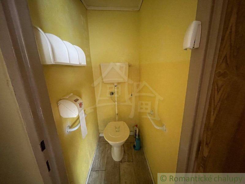 A small bathroom with a toilet in a family house, yellow walls and wooden floor.