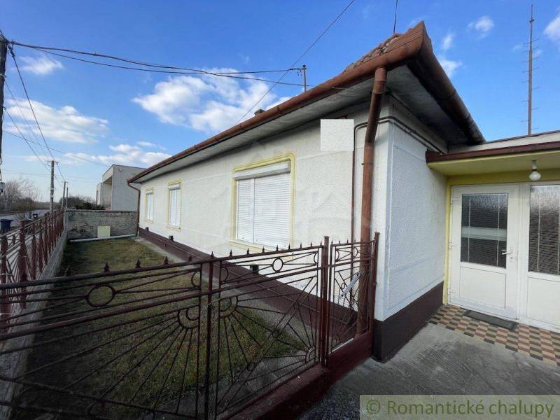 A family house in Nové Zámky with a garden behind a metal fence under a blue sky.