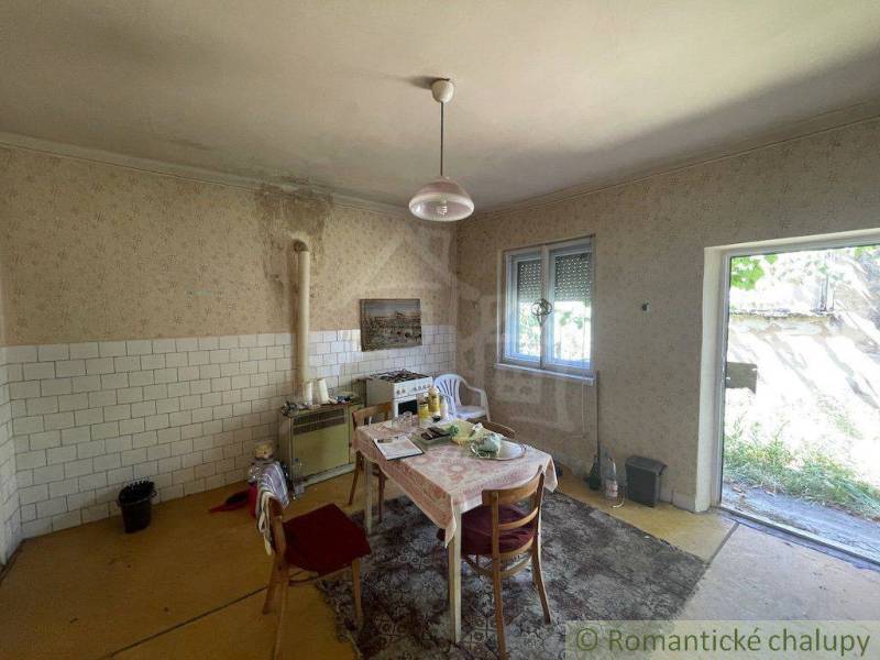 Interior of a family house with older furniture, a kitchen table, and open doors to the garden.