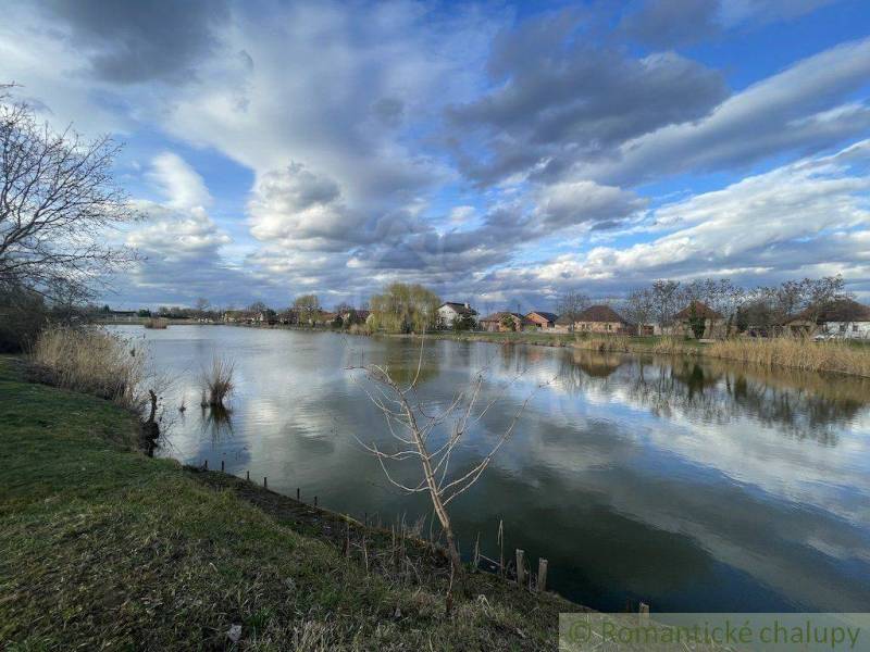Idyllic landscape with a lake, clouds, and family houses in the background by the shore.
