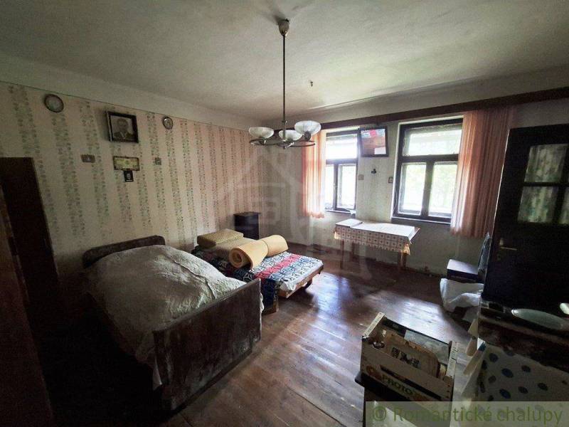 A room in a family house with a bed, wooden floor, and patterned wallpaper.