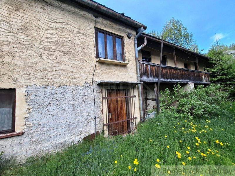 A family house in Pohorelá, stone walls, wooden balcony, surrounded by greenery and flowers.