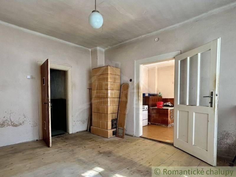 A room with a tiled stove, wooden floor, and kitchen in a family house.