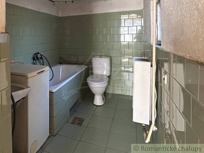 A bathroom in a family house with a bathtub, toilet, and washing machine with tiles.
