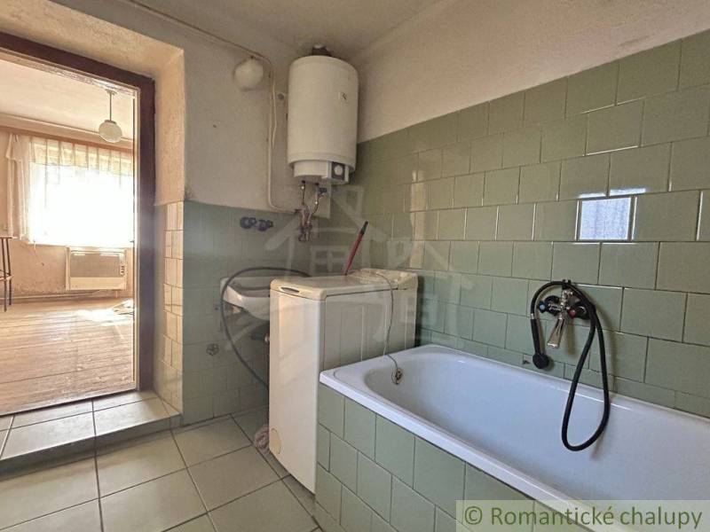 A family house bathroom with a bathtub, washing machine, and green tiles.