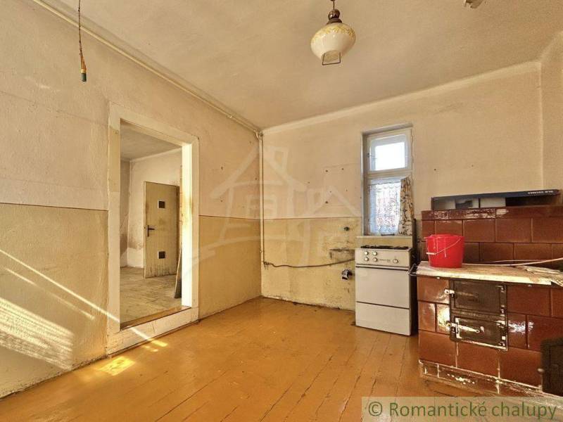 A room with a tiled stove and a cooker in a family house, wooden floor and simple furnishings.