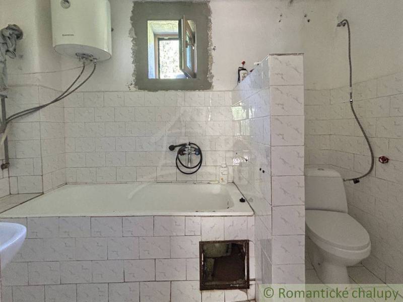 A bathroom in a family house with a bathtub, toilet, and gas water heater.
