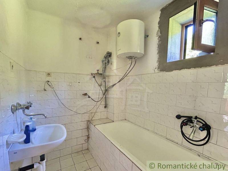 A simple bathroom in a family house with a bathtub and a boiler on the wall.