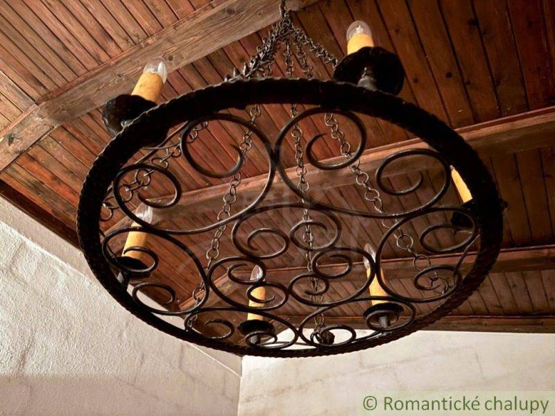A wrought iron lamp with candles in the interior of a family house with a wooden ceiling.