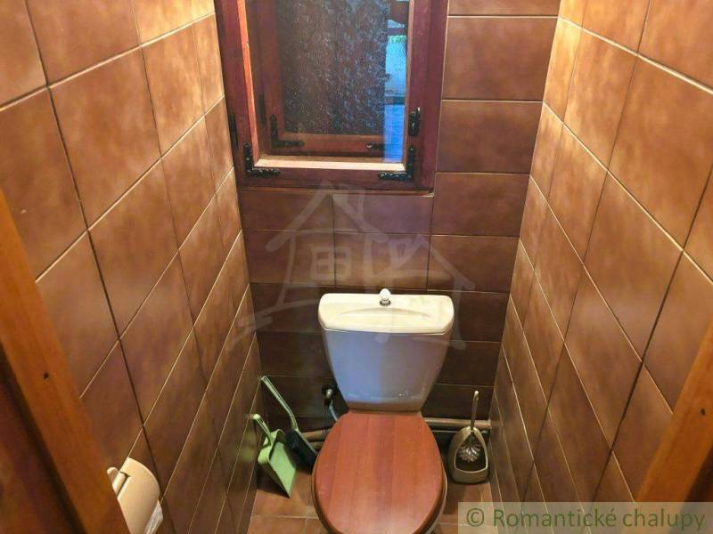 A small toilet in a family house with a wooden window and brown tiles.