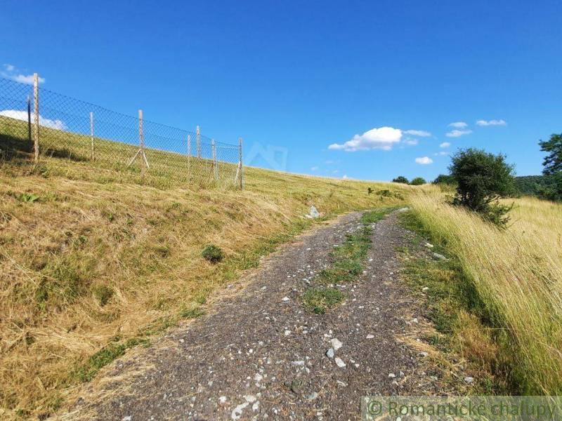 A dirt road in the Gardens in Žarnovica, surrounded by grassy slopes and a fence.