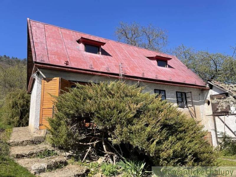 A cottage in Rožňava with a red roof, surrounded by lush greenery and a clear sky.