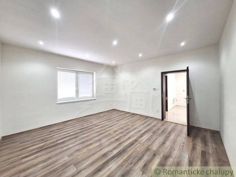 A room with a wooden floor and a window in a family house, neutral tones, ceiling lights.