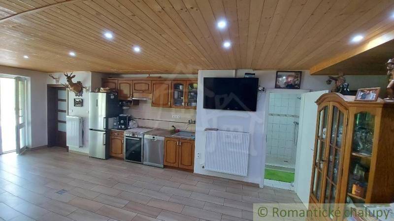 A kitchen in a family house with a wooden ceiling, kitchen unit, and a television on the wall.