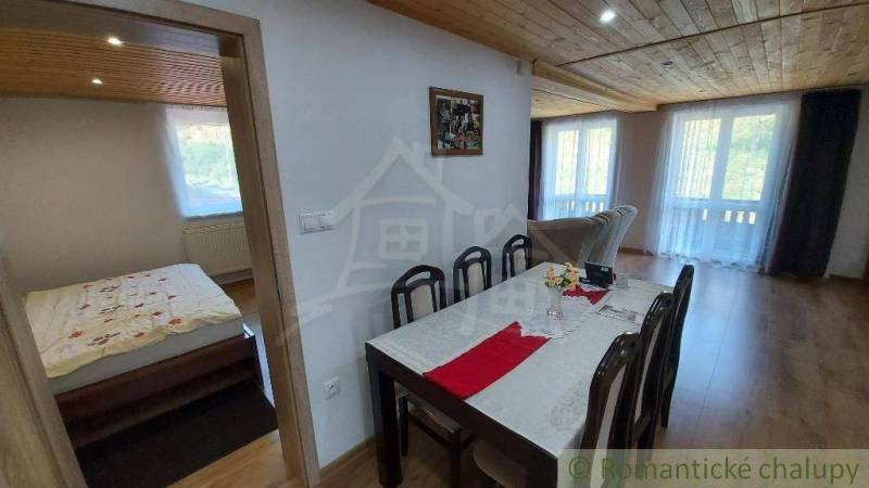 A dining room with a wooden ceiling, a set table, and an open passage to the bedroom in a family house.