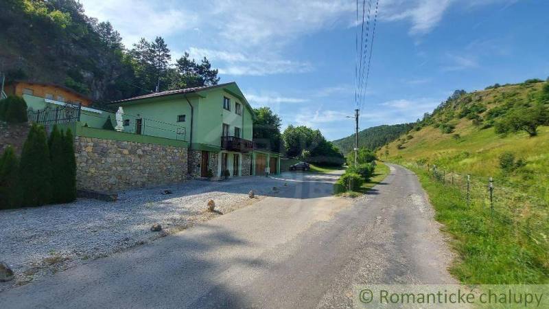 A family house in Dobrá Voda by the road surrounded by green hills and trees.