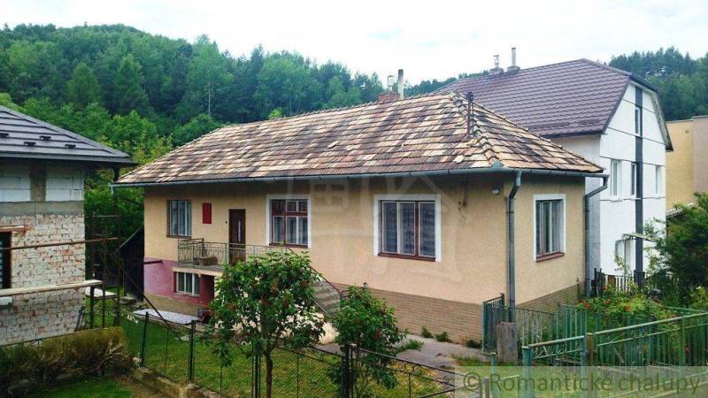 A family house in Fričovce with a sloped roof, garden, and surrounding forest.
