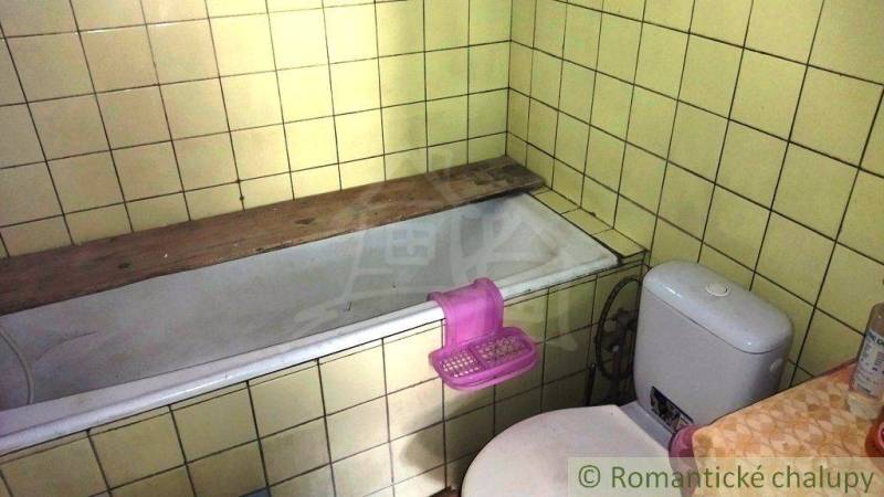 A bathroom in a family house with a bathtub and toilet, surrounded by yellow tiles.