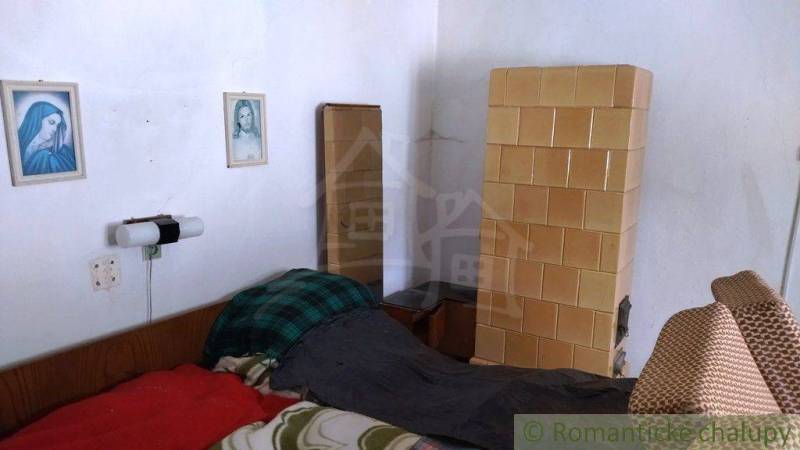 A room in a family house with a tiled stove, a bed, and wall pictures.