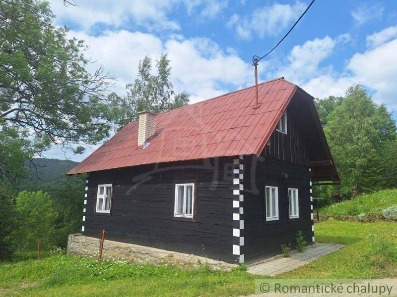 A traditional wooden cottage in Klokočov with a red roof, surrounded by greenery and trees.