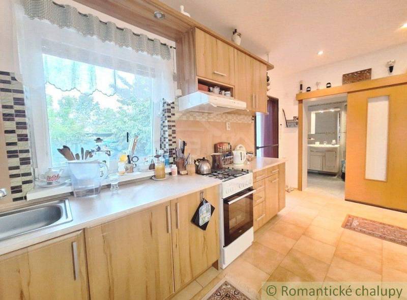 A kitchen in a family house with wooden cabinets, a stove, and a view through a large window.