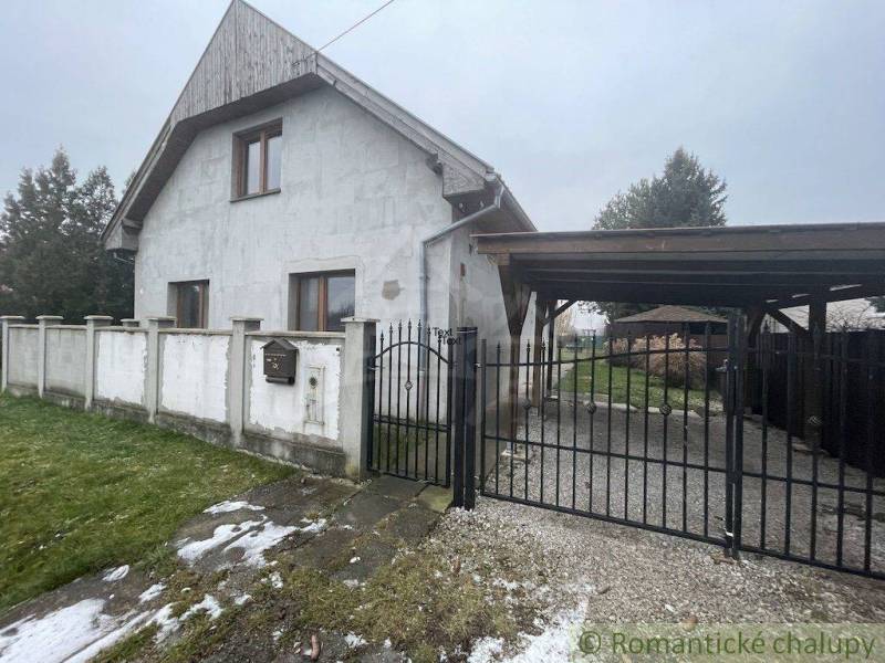 A family house with a white facade and gate, surrounded by a lawn and fencing.