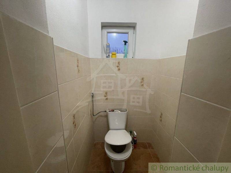 A small bathroom with ceramic tiles, a toilet, and a window in a family house.