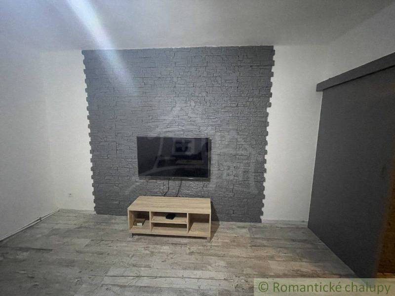 A television on a stone wall, with a wooden table underneath, in a room in a family house.