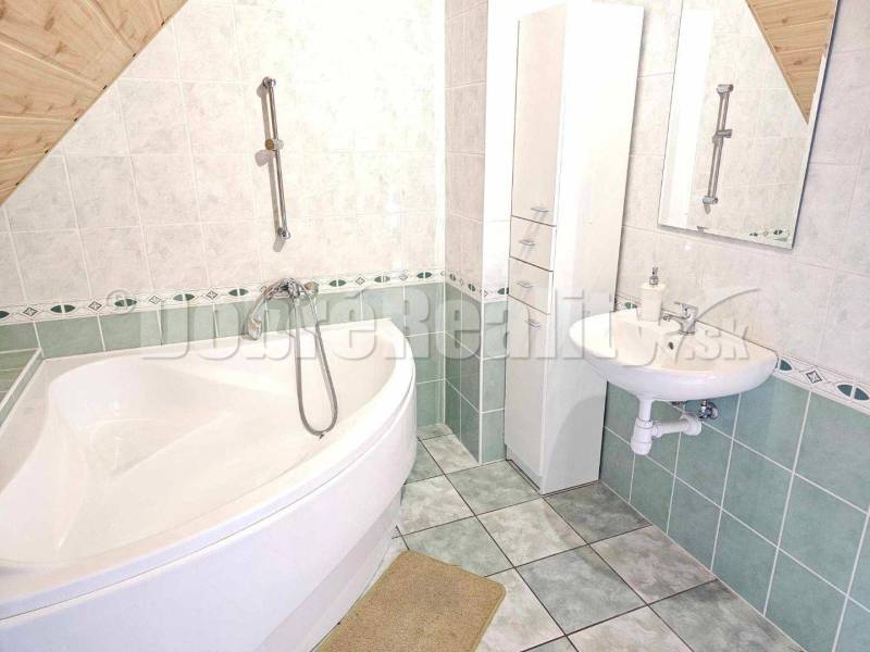A bathroom in a family house with a corner bathtub, a sink, and green and white tiles.