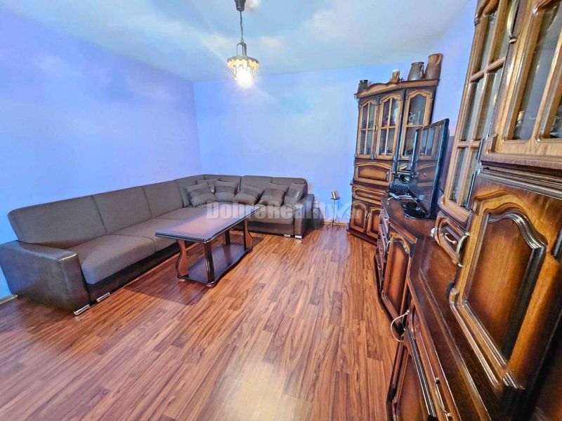 Living room of a family house with a wooden decor floor, a sofa, and dark wood furniture.