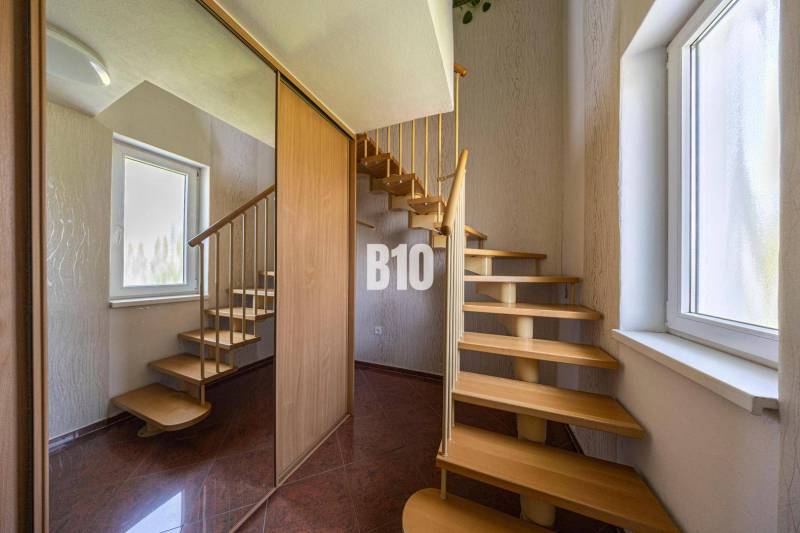 A staircase in a family house with wooden steps, a large window, and a mirrored wall.
