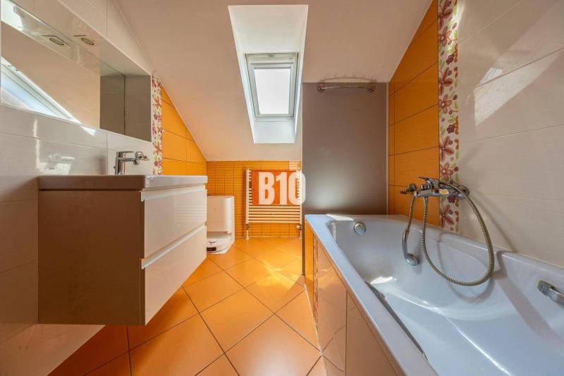 A bathroom in a family house with orange tiles, a bathtub, a sink, and a skylight.
