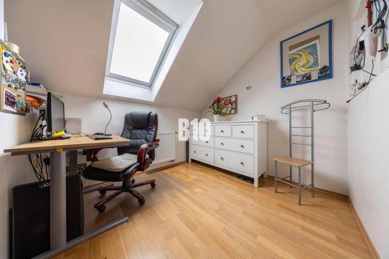 A study in a family house with a desk, an armchair, and a chest of drawers under a skylight.